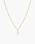 Collar Pearl Drop, colgante de una sola perla blanca ovalada en una cadena fina de bolitas en tono dorado, sobre fondo blanco