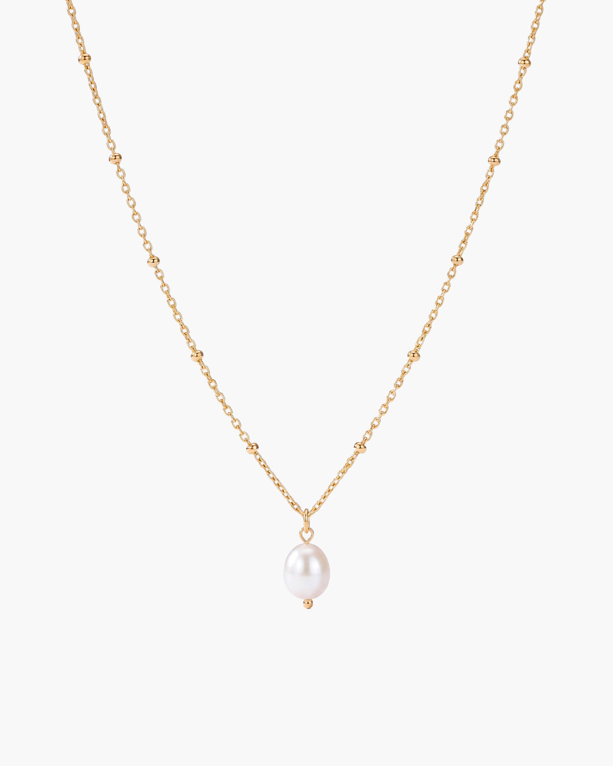 Collar Pearl Drop, colgante de una sola perla blanca ovalada en una cadena fina de bolitas en tono dorado, sobre fondo blanco