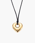 Collar Amara, colgante pulido de corazón abombado en tono dorado con el centro abierto en cordón negro encerado, sobre fondo blanco