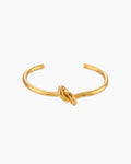 Brazalete Nudo, brazalete abierto en tono dorado con un nudo pulido en el centro, vista frontal sobre fondo blanco